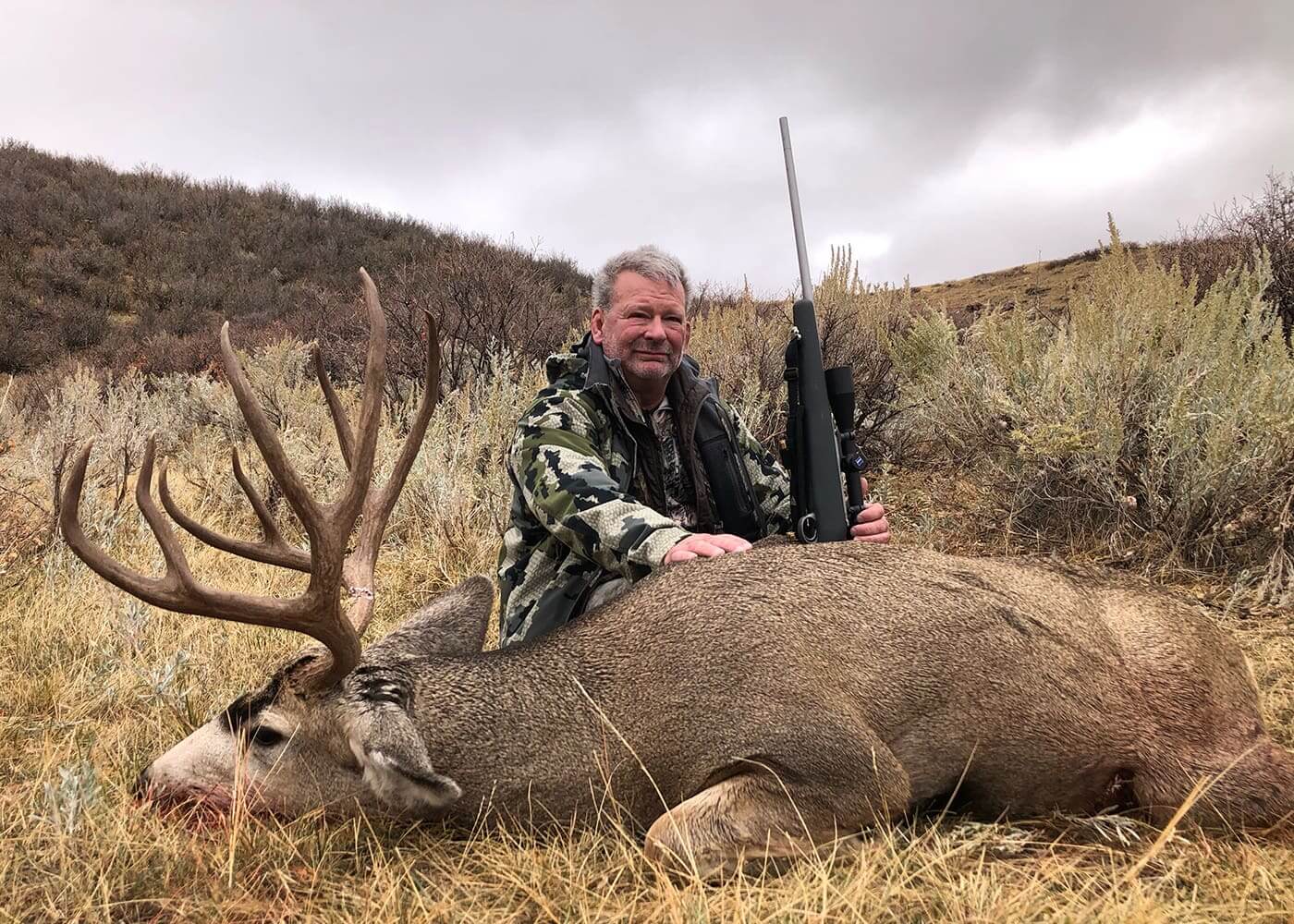 Man posing with a large deer and rifle in a field