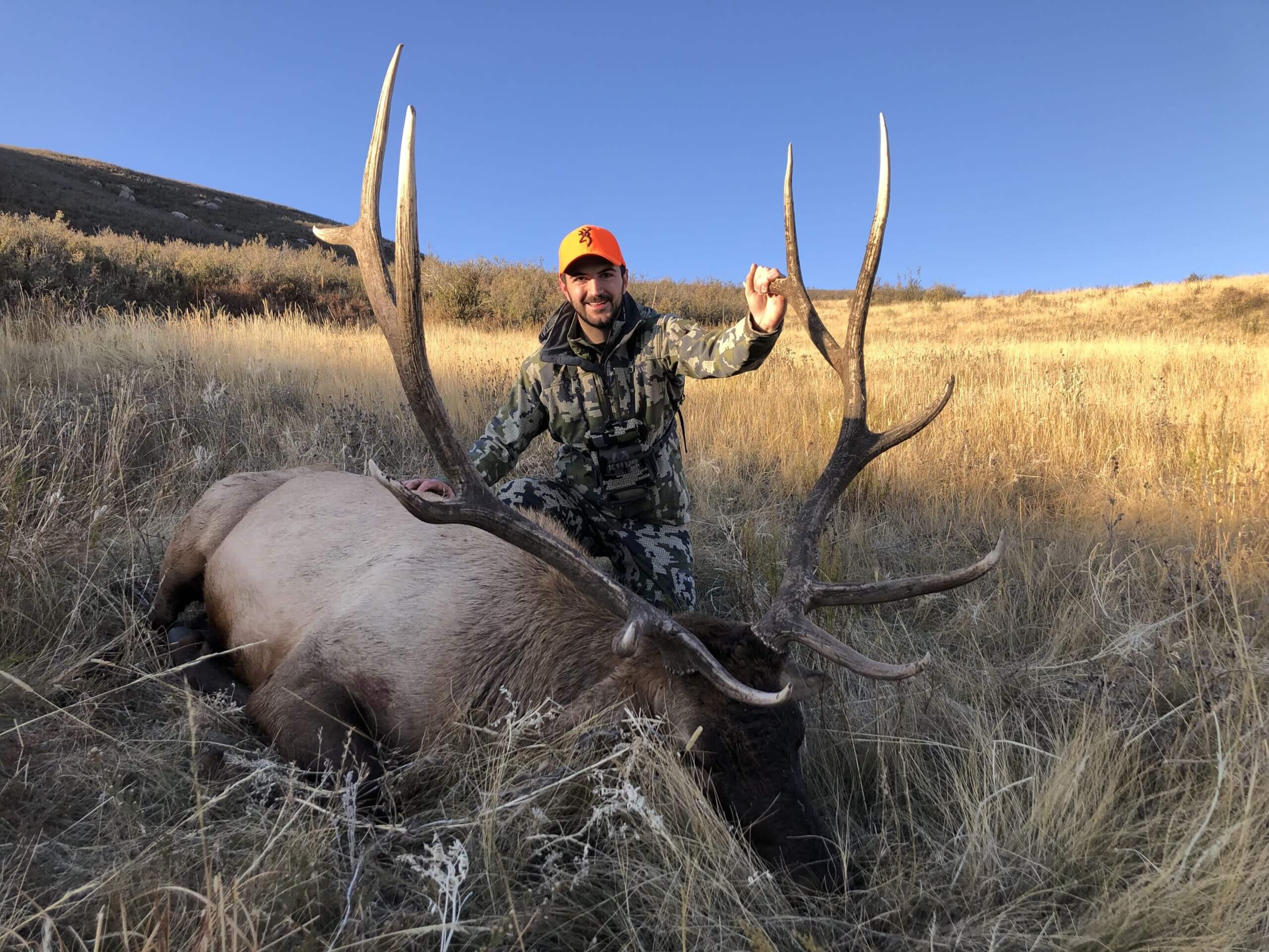 Man holding an elk's antlers in a field with a clear sky