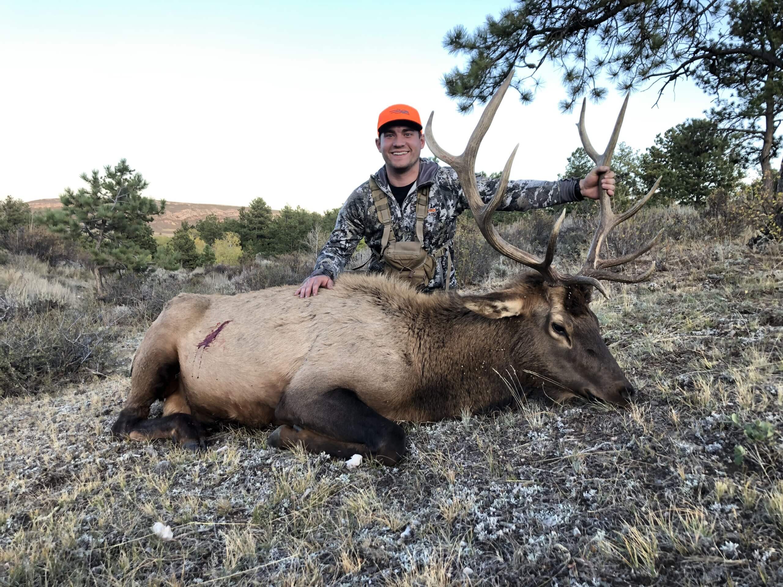Hunter posing with a large elk in a natural landscape