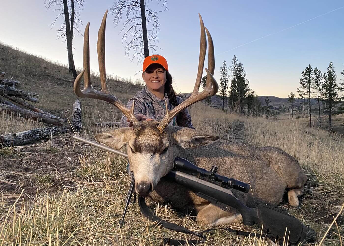 Huntress with a large deer and rifle in a natural setting