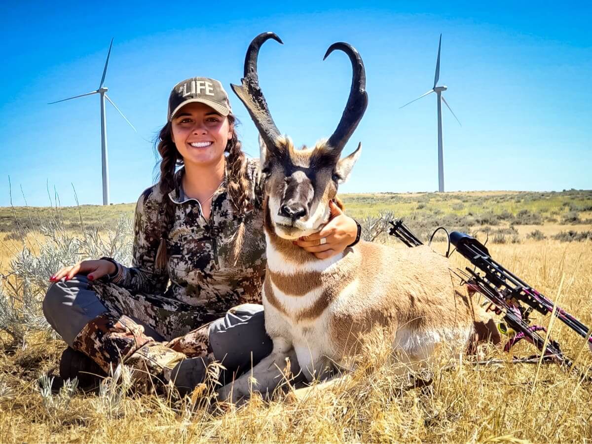 Woman holding a hunted antelope with wind turbines in the background