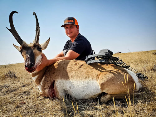 Man posing with a hunted antelope in a field
