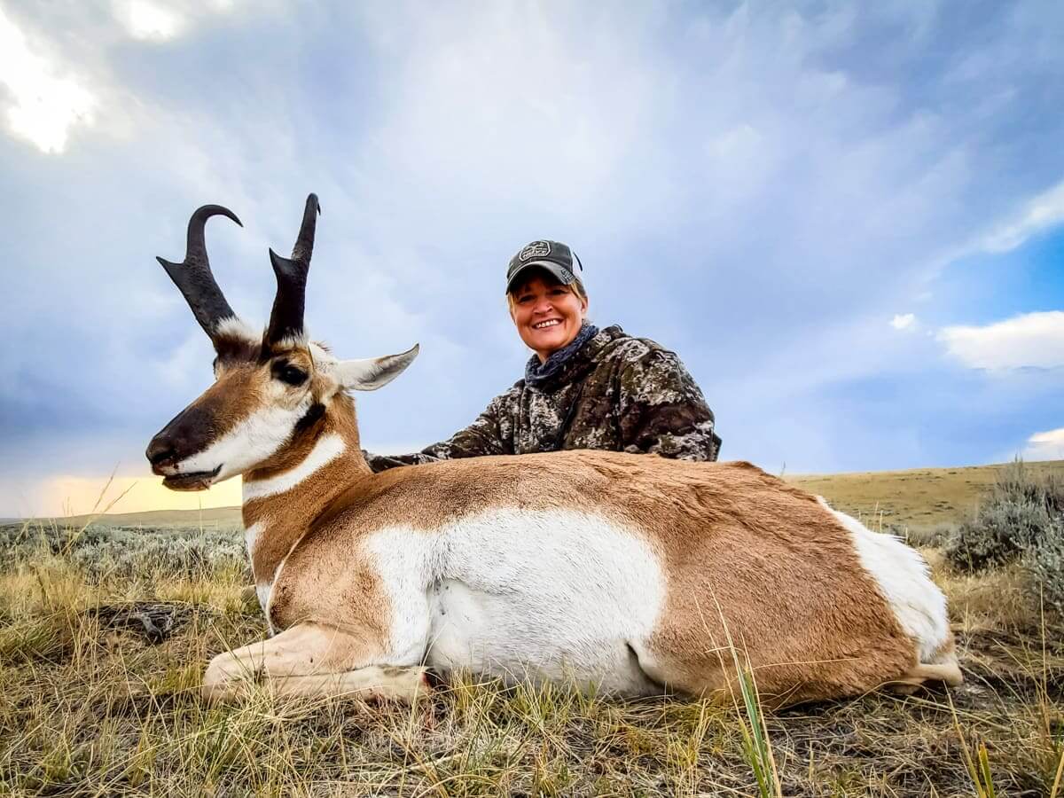 Person posing with a hunted antelope in a grassy field