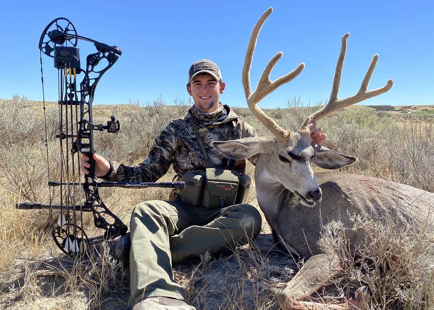 Hunter with a bow and a large deer in a desert landscape