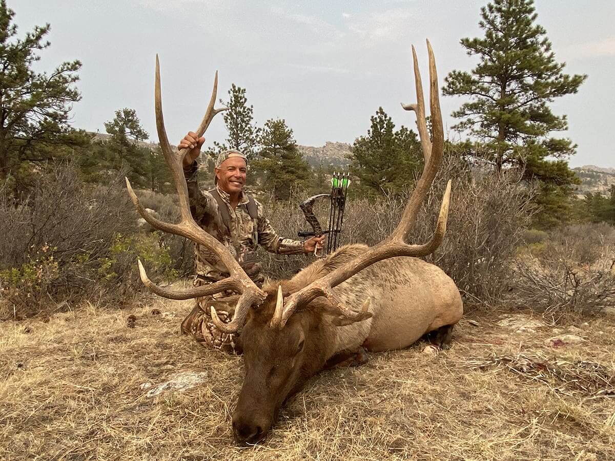 Huntress posing with a large elk in a forested area
