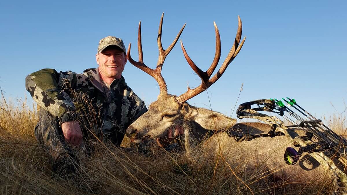 Hunter with a large deer and bow in a field