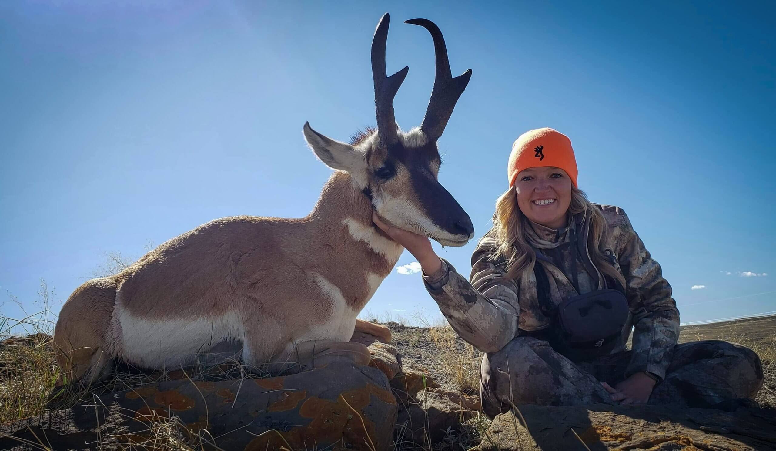 Person in camouflage clothing with a hunted pronghorn antelope on a clear day.